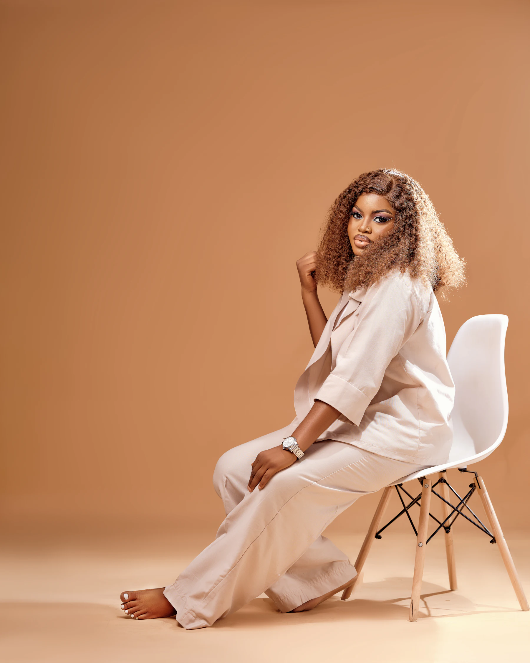Woman in neutral loungewear seated on a chair against a warm terracotta backdrop